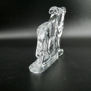 May include: A clear glass sculpture of a camel, with a textured surface. The sculpture is standing on a rectangular base. The camel is facing to the left.