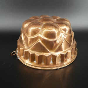 May include: A vintage copper jelly mould with a decorative, fluted design. The mould has a rounded top with a series of raised, rounded bumps.