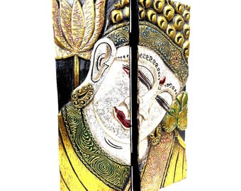 Puede incluir: Un panel de pared de madera de dos piezas con un rostro de Buda tallado dividido entre los paneles. El diseño incluye pintura dorada, verde y blanca sobre un fondo negro, mostrando una flor de loto y patrones intrincados en las túnicas.