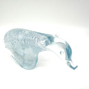 May include: A clear glass figurine shaped like a polar bear in a walking pose. The body features a textured, frosted interior finish that contrasts with the smooth, transparent glass of the head and neck area, creating a light blue tint.