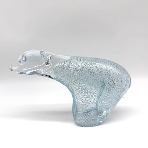 May include: A clear glass polar bear figurine with a textured, frosted body and a smooth, transparent head. The sculpture features a distinct contrast between the rough, icy-looking surface of the torso and the polished, clear glass of the face.