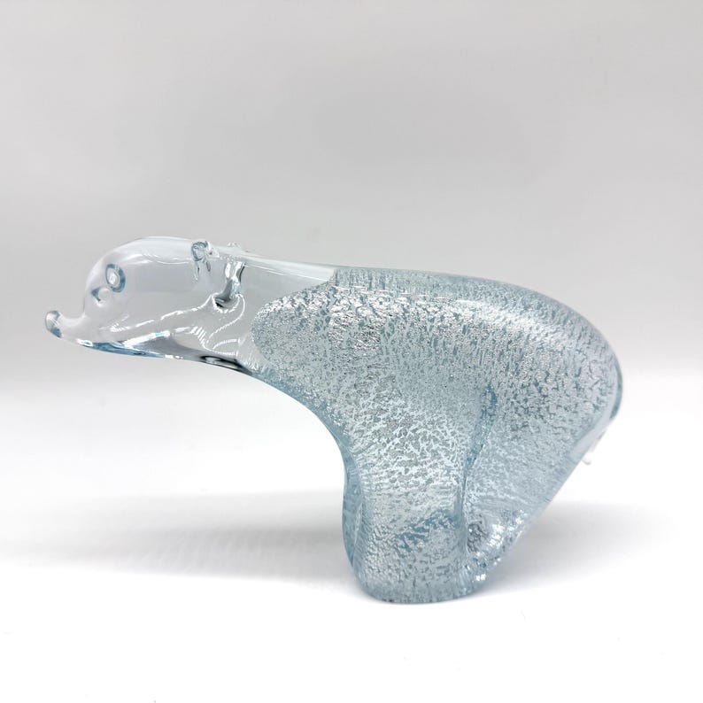 May include: A clear glass polar bear figurine with a textured, frosted body and a smooth, transparent head. The sculpture features a distinct contrast between the rough, icy-looking surface of the torso and the polished, clear glass of the face.