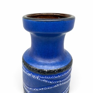 May include: A cylindrical ceramic vase with a vibrant blue matte finish, featuring a wide flared rim, a dark brown interior, and a textured black band around the center. The lower section displays a white speckled diagonal pattern.