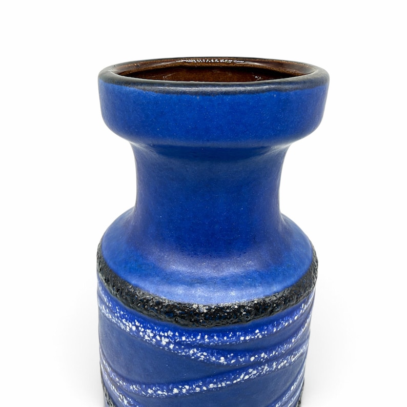 May include: A cylindrical ceramic vase with a vibrant blue matte finish, featuring a wide flared rim, a dark brown interior, and a textured black band around the center. The lower section displays a white speckled diagonal pattern.