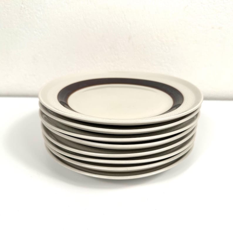 May include: A stack of ten white ceramic plates with a brown band around the edge.