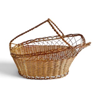 Puede incluir: Una cesta de alambre met&aacute;lico en tono dorado con base ovalada y un patr&oacute;n de celos&iacute;a trenzada en los laterales. La cesta incluye un asa &uacute;nica de alambre trenzado arqueado unida al borde, con un marco abierto extendido en un lado.