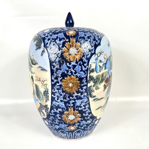 Puede incluir: Un tarro de jengibre de cer&aacute;mica con tapa que presenta un fondo azul oscuro con intrincados patrones florales en azul claro y dorado. El tarro tiene dos paneles ovalados que representan escenas pintadas de figuras en un paisaje.