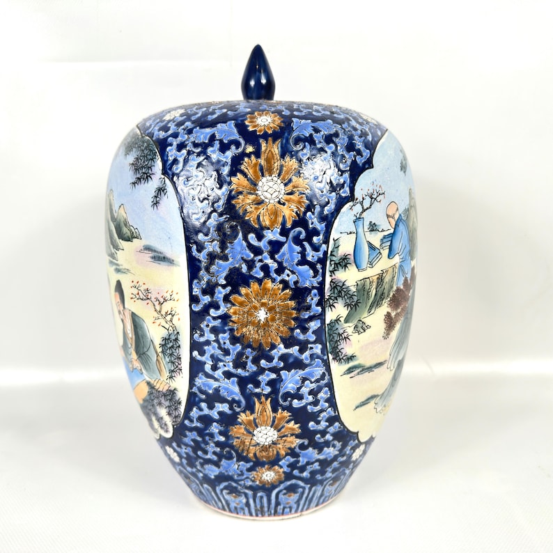 Puede incluir: Un tarro de jengibre de cer&aacute;mica con tapa que presenta un fondo azul oscuro con intrincados patrones florales en azul claro y dorado. El tarro tiene dos paneles ovalados que representan escenas pintadas de figuras en un paisaje.