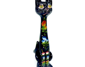 May include: A tall, black cat figurine with a slender body and floral painted details. The cat has yellow eyes, a pink nose, and is decorated with colorful flowers in red, orange, blue, and green. The figurine is hand-painted.