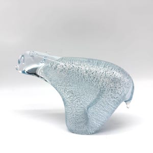 May include: A clear glass figurine of a polar bear in a walking pose. The body of the bear features a textured, bubbled interior finish that creates a shimmering, icy appearance, while the head and limbs are made of smooth, transparent glass.