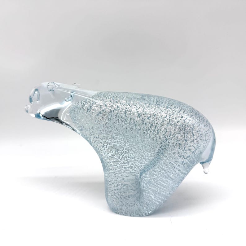 May include: A clear glass figurine of a polar bear in a walking pose. The body of the bear features a textured, bubbled interior finish that creates a shimmering, icy appearance, while the head and limbs are made of smooth, transparent glass.