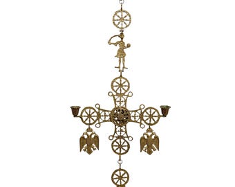 Può includere: Un candelabro sospeso in metallo color oro caratterizzato da una struttura a croce centrale con filigrana complessa, motivi a ruota circolari, una figura in piedi in alto e due pendenti a aquila bicipite accanto a due portacandele.