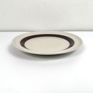 May include: A white ceramic plate with a brown band around the edge.