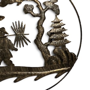 May include: A circular metal wall art piece featuring a dark bronze finish with a textured surface. The design depicts a figure carrying a spiky object on a pole, a gnarled tree, and a multi-tiered pagoda structure, all enclosed within a thin metal frame.