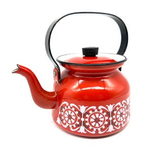 May include: A red enamel kettle with a black handle and lid. The kettle has a white and black floral pattern around the base. The spout is curved and the lid has a black knob. A classic kitchenware item.