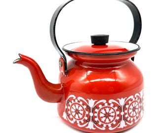 May include: A red enamel kettle with a black handle and lid. The kettle has a white and black floral pattern around the base. The spout is curved and the lid has a black knob. A classic kitchenware item.