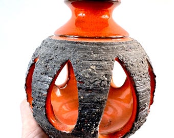 Puede incluir: Un jarrón de cerámica esférico con un interior naranja liso y brillante y un exterior texturizado de color gris carbón. La superficie exterior tiene recortes verticales que revelan el esmalte naranja brillante, con una abertura de cuello ensanchada.