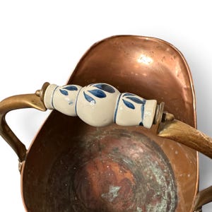 Pu&ograve; includere: Un secchio per carbone in rame con manico in metallo curvo e impugnatura centrale in ceramica. Il manico in ceramica &egrave; color bianco sporco con un motivo a foglie blu dipinto a mano. L'interno del contenitore in rame presenta ossidazione.