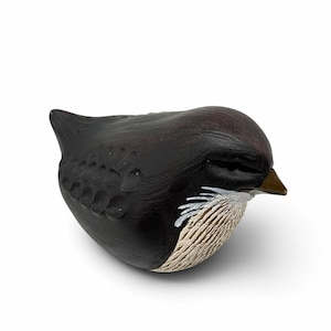 May include: A small, rounded bird figurine crafted with a dark brown, matte finish. The sculpture features carved, scale-like textures on the wings and a contrasting cream-colored, textured chest area. It has a small, pointed brown beak.