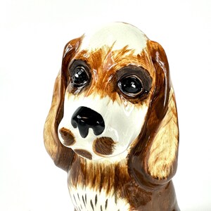 Peut inclure: Figurine de chien en c&eacute;ramique, marron et blanc. Le chien a de grands yeux noirs, un nez noir et de longues oreilles tombantes. Objet d&eacute;coratif, probablement destin&eacute; &agrave; &ecirc;tre expos&eacute;.