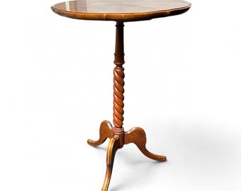 May include: A brown wooden pedestal table featuring a smooth, circular tabletop surface. The central support column displays a distinct spiral twist design, resting on a tripod base with three curved legs that extend outward for stability.