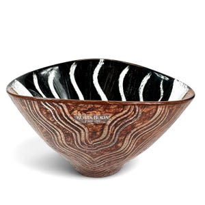 May include: A Kosta Boda glass bowl with a brown exterior featuring a textured, swirling wood-grain pattern. The interior is black with vertical, white, brushstroke-like lines radiating from the center toward the rim of the bowl.