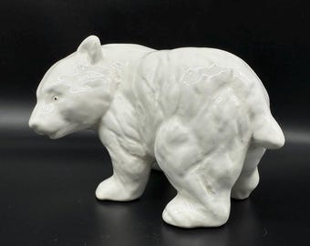 May include: A white ceramic bear figurine. The bear is depicted in a walking pose, with detailed fur texture and a glossy finish. The figurine is a decorative item, suitable for display.