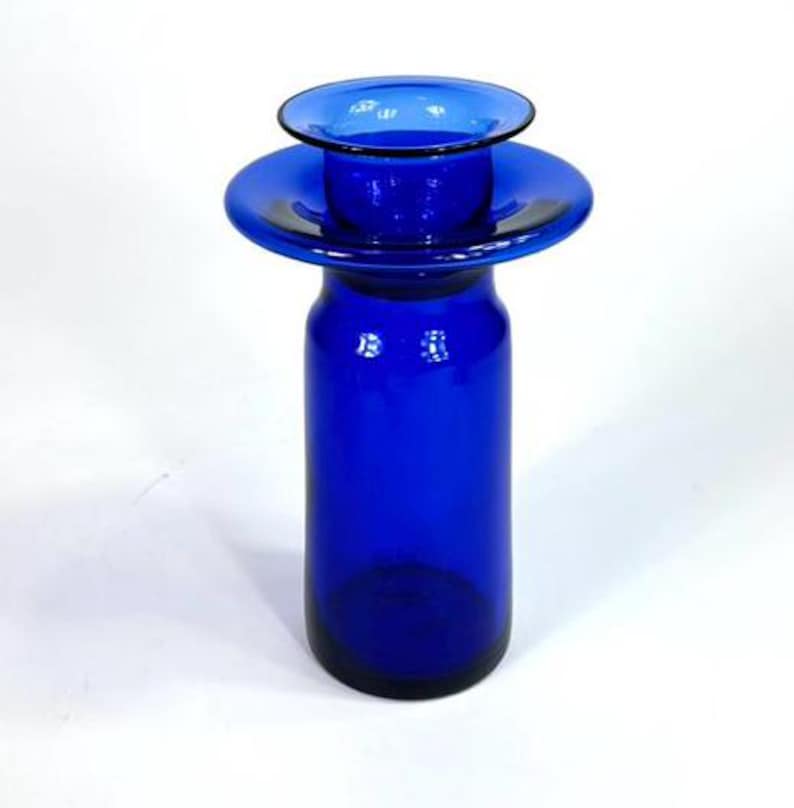 Op de afbeelding: Een kobaltblauwe glazen vaas met een brede, platte bovenkant en een cilindrische basis. De vaas is gemaakt van dik glas en heeft een gladde, gepolijste afwerking.