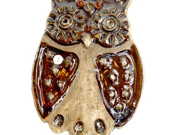 May include: A glazed ceramic owl wall plaque featuring a glossy dark brown finish on the eyes and wings, contrasted by a lighter tan textured body. The wings are decorated with small, raised circular indentations. A small white circular sticker is visible.
