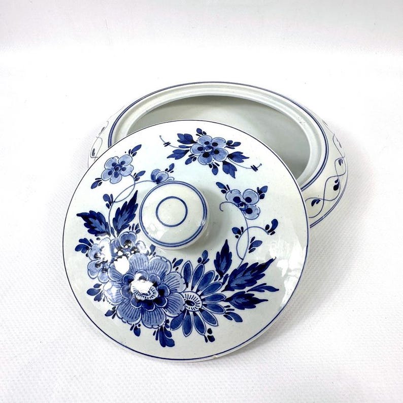 May include: A white ceramic serving dish with a lid, decorated with blue floral patterns. The lid has a central knob and a detailed floral design. The dish's rim is also decorated with blue accents, creating a cohesive and elegant appearance.