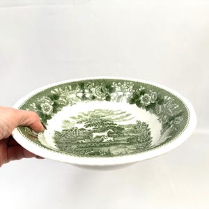 May include: White ceramic serving bowl with a green pastoral scene and floral border. The bowl features a detailed landscape with trees, animals, and a building. The rim has a scalloped edge.