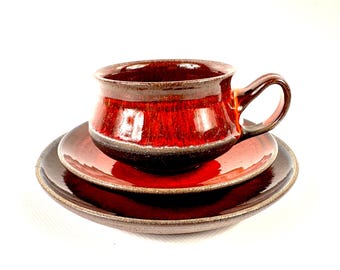 Peut inclure: Service à thé en céramique rouge et marron composé d'une tasse avec anse et de deux soucoupes assorties. La finition brillante met en valeur les couleurs riches et les textures de la poterie artisanale.