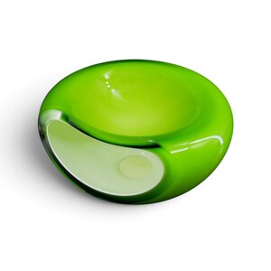 May include: A smooth, rounded glass bowl featuring a vibrant lime green exterior that transitions into a clear, transparent interior. The object has a wide, circular opening at the top and a secondary side-facing aperture, creating a hollow form.