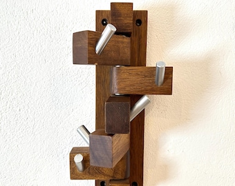 May include: A wall-mounted coat rack featuring a vertical dark brown wooden base with multiple pivoting rectangular wooden blocks. Each block is fitted with a cylindrical silver metal hook, allowing for adjustable positioning of the hooks.