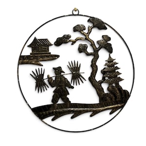 May include: A circular black and gold metal wall art piece featuring a silhouette of a person carrying two bundles on a pole across their shoulders. The scene includes a small building, a pagoda, and a tree, all enclosed within a thin metal ring.