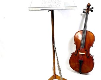 May include: A wooden music stand with sheet music, a cello, and a silver flute. The cello is brown with black strings. The flute is silver. The music stand is brown with a wooden base. The sheet music is white with black notes.
