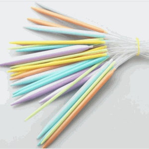 May include: A set of colorful knitting needles in various pastel shades, including orange, yellow, blue, and purple. The needles are bundled together and secured with a clear plastic band.