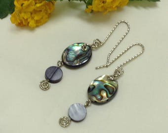Peut inclure: Une paire de boucles d'oreilles en argent avec une coquille d'ormeau ovale irisée et des perles rondes violettes. Les boucles d'oreilles pendent d'une chaîne en argent.