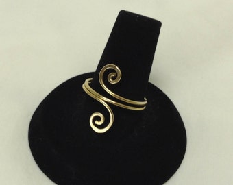 May include: A gold ring with a double spiral design, displayed on a black ring stand.