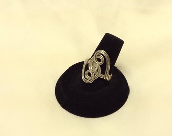 May include: A silver wire ring with a swirling design. The ring is displayed on a black velvet ring holder.