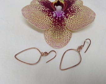 Peut inclure: Une paire de boucles d'oreilles en or rose en forme de larme. Les boucles d'oreilles sont présentées sur un fond blanc avec une orchidée jaune et violette.