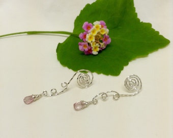 Peut inclure: Une paire de boucles d'oreilles argentées avec des accents de cristal rose. Les boucles d'oreilles sont en fil de fer et ont un design en spirale.