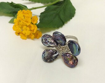 Peut inclure: Une bague en argent avec un motif de fleur composé de perles noires irisées. Les perles sont reliées par du fil pour former une fleur.