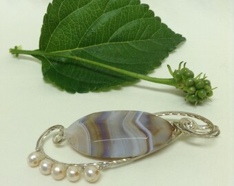 Peut inclure: Un pendentif en argent avec une pierre d'agate bleu clair, marron et blanche. Le pendentif est attaché à une chaîne en argent avec un motif en spirale et une rangée de perles blanches.