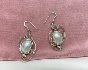 Peut inclure: Une paire de boucles d'oreilles en argent avec une pierre blanche nacrée sertie dans un motif de fil.
