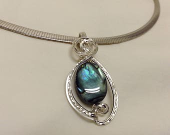 Peut inclure: Un collier en chaîne argent avec un pendentif argenté orné d'une coquille d'ormeau bleue et verte.