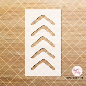 May include: A white stencil with four upward-pointing arrow shapes cut out. The stencil is rectangular and sits on a light brown wooden surface with a diamond pattern. The text "Textile Bakery COPYRIGHT 2023" is visible.