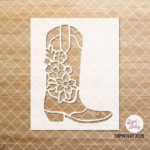 May include: A white stencil of a cowboy boot with floral designs on the side. The stencil is on a woodgrain background. COPYRIGHT 2025 is printed at the bottom of the stencil.