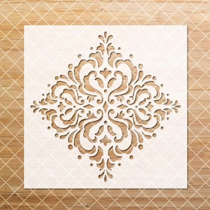 May include: A white stencil with a decorative, intricate, symmetrical design. The design is a diamond shape with a floral pattern.