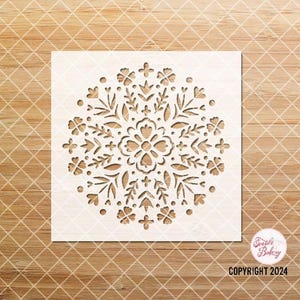 May include: White stencil with a floral mandala design. The design features a large central flower surrounded by smaller flowers, leaves, and dots. The stencil is perfect for creating decorative patterns on cakes, cookies, and other surfaces.